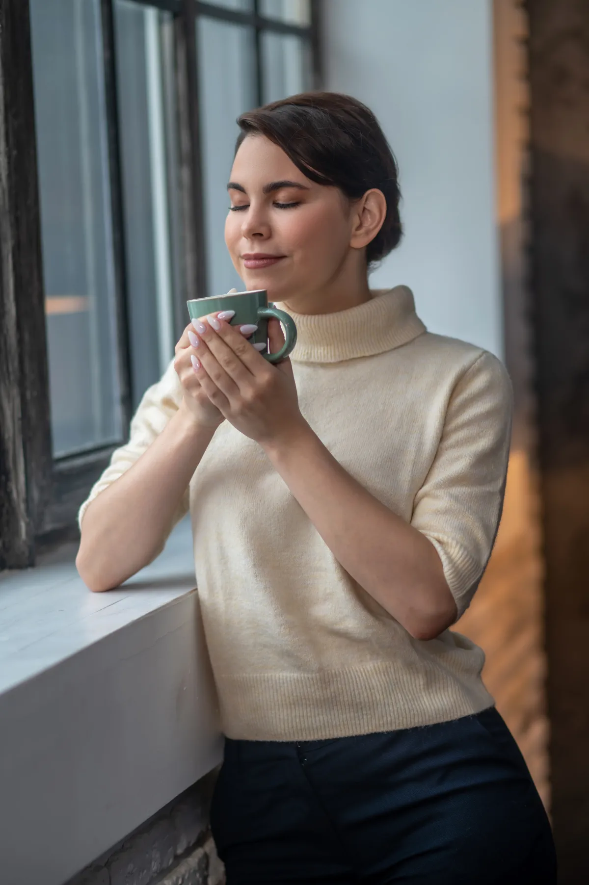 Mulher com uma caneca junto à janela, em um momento de calma